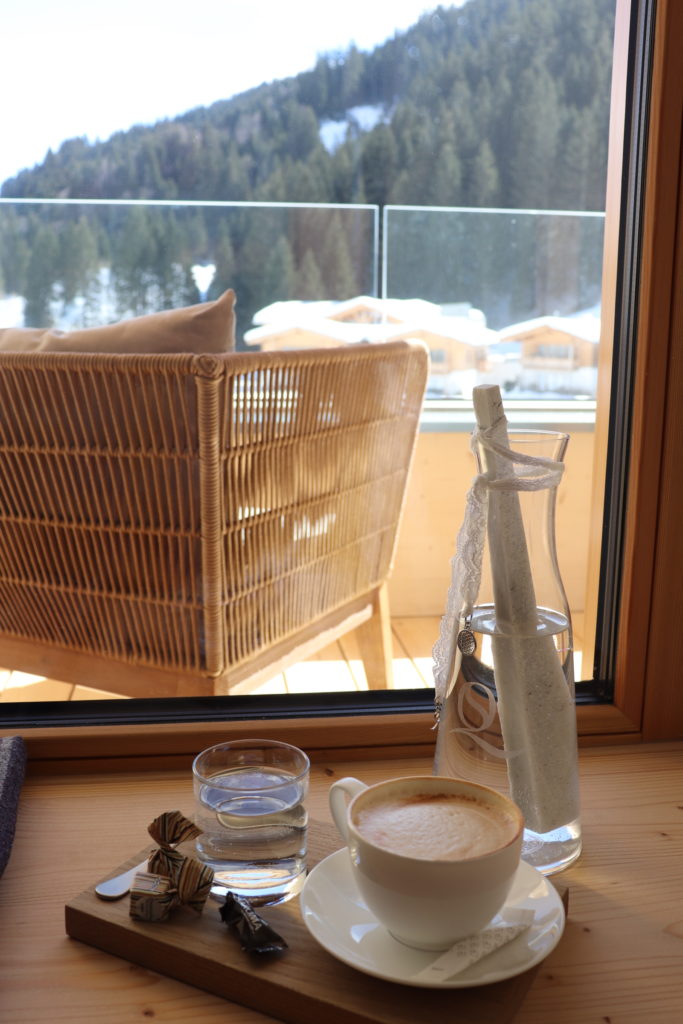 Tablett mit Kaffee und Wasserflasche am Zimmerfenster mit Bergblick