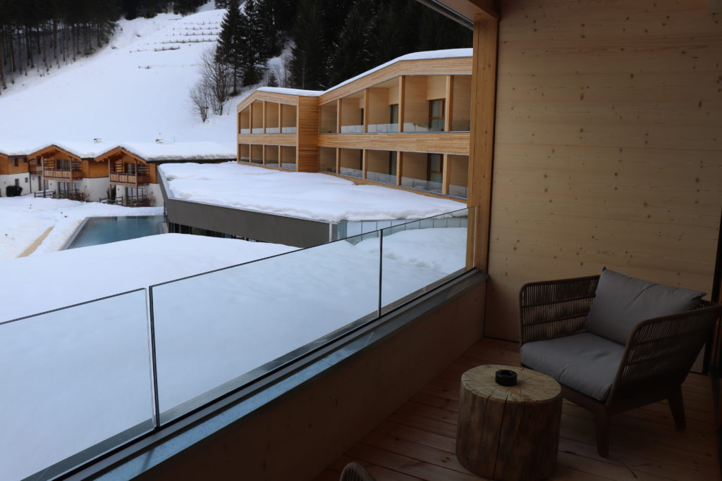 Balkon mit Sessel und Blick auf Pool und Chalets im Schnee