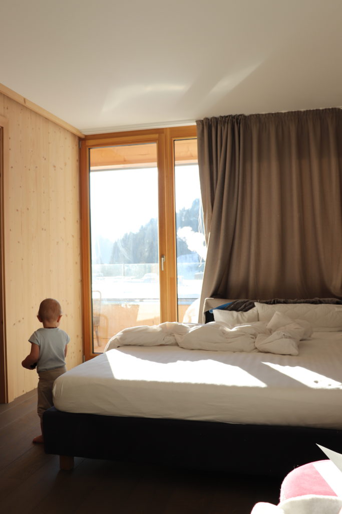 Kind am Fenster des Hotelzimmers mit Bergblick