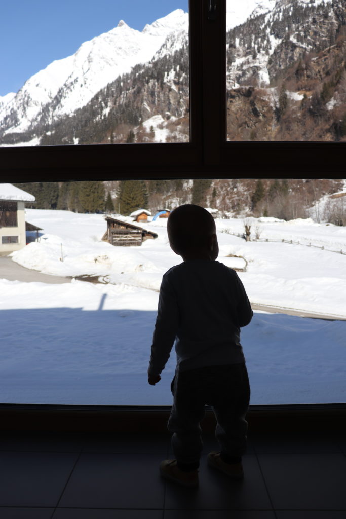 Kind am Panoramafenster mit Blick auf die verschneiten Berge