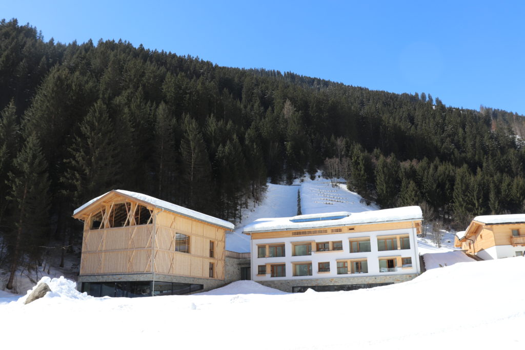 Resortgebaeude im Schnee vor bewaldetem Hang
