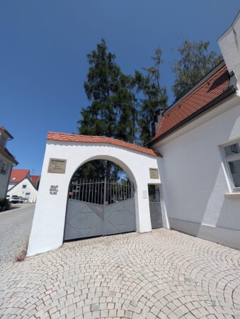Weißes Eingangstor zum jüdischen Friedhof Laupheim mit der Inschrift Bestelle dein Haus