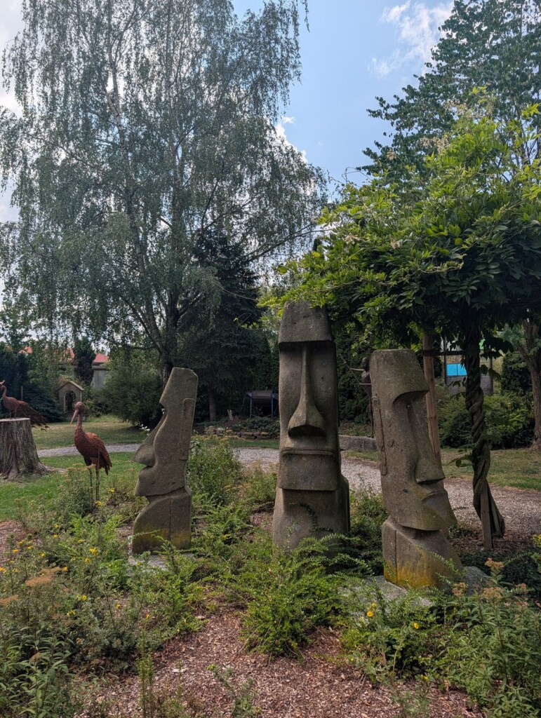 Steinfiguren zwischen Baeumen im Garten