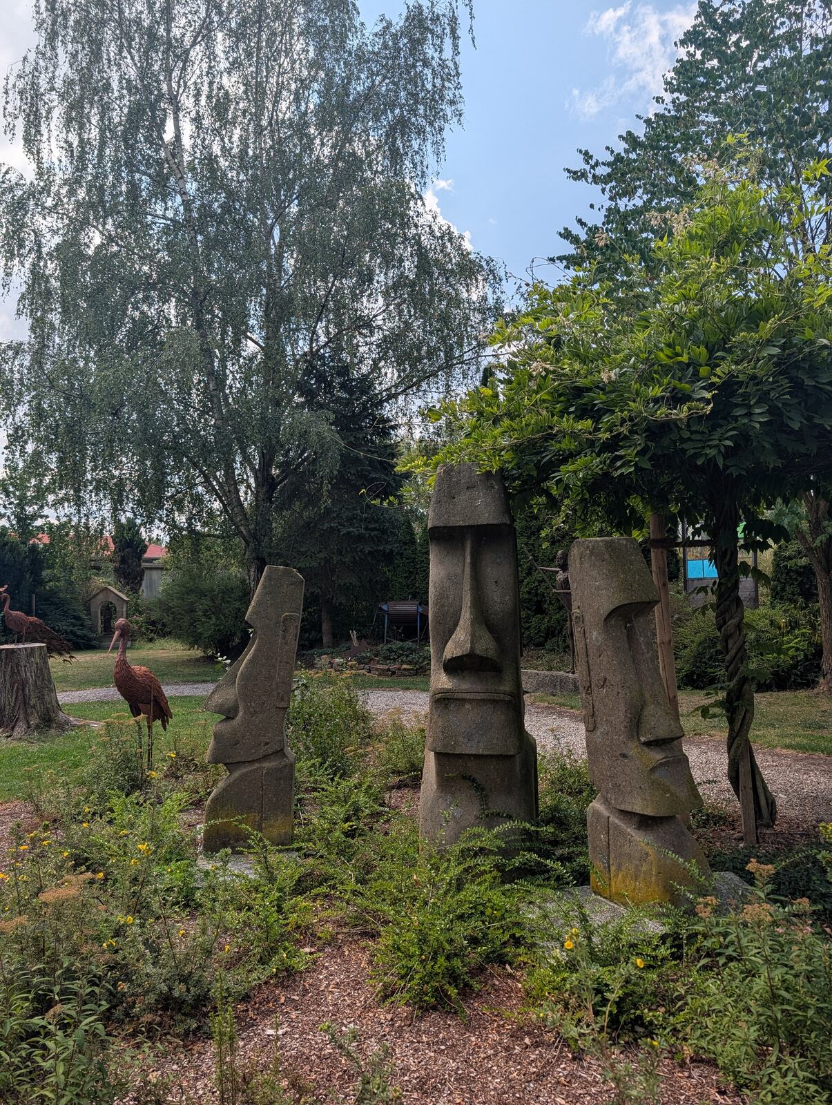 Steinfiguren zwischen Baeumen im Garten