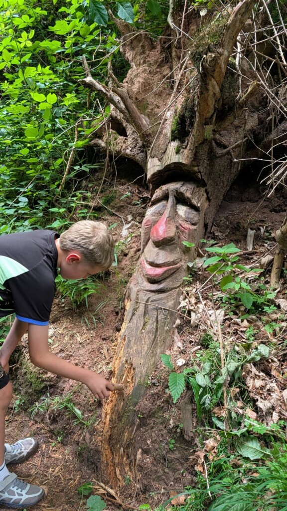 Kind entdeckt eine Holzfigur am Wegrand