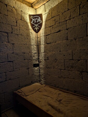 Steinerner Raum mit beleuchtetem Katzenwappen und Bett auf Burg Katzenstein