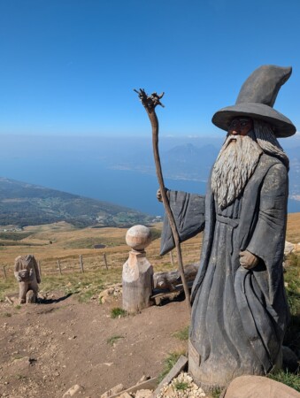 Geschnitzte Holzfigur eines Zauberers am Monte Baldo, dahinter der Gardasee