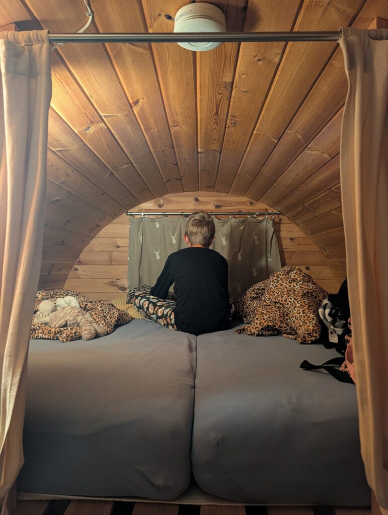Doppelbett im Schlaffass mit runder Holzdecke, Kind sitzt auf dem Bett
